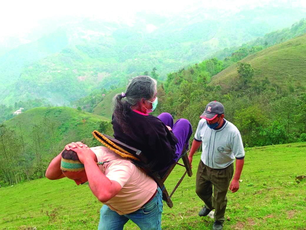 A la vieja usanza, un hombre transporta en una silla sujetada a su espalda, a una adulta mayor hacia el centro de vacunación en Tenango de Doria, en la región Otomí-Tepehua.